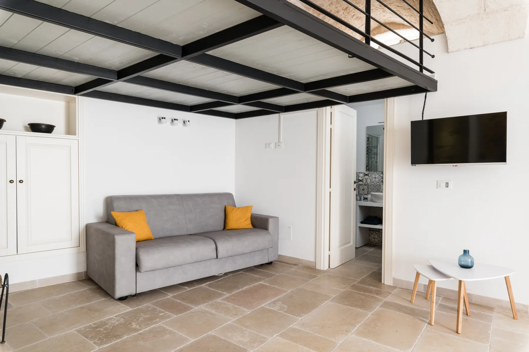 Sala de estar con sofá gris, televisor en la pared y un altillo encima.