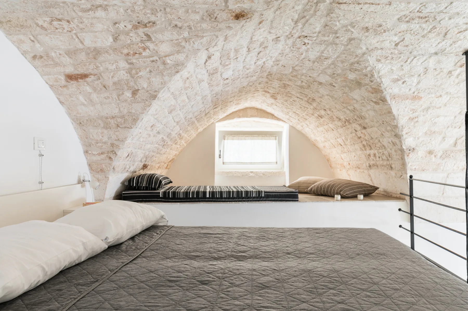 Una zona baja para dormir bajo un techo curvo de piedra, con una ventana pequeña.