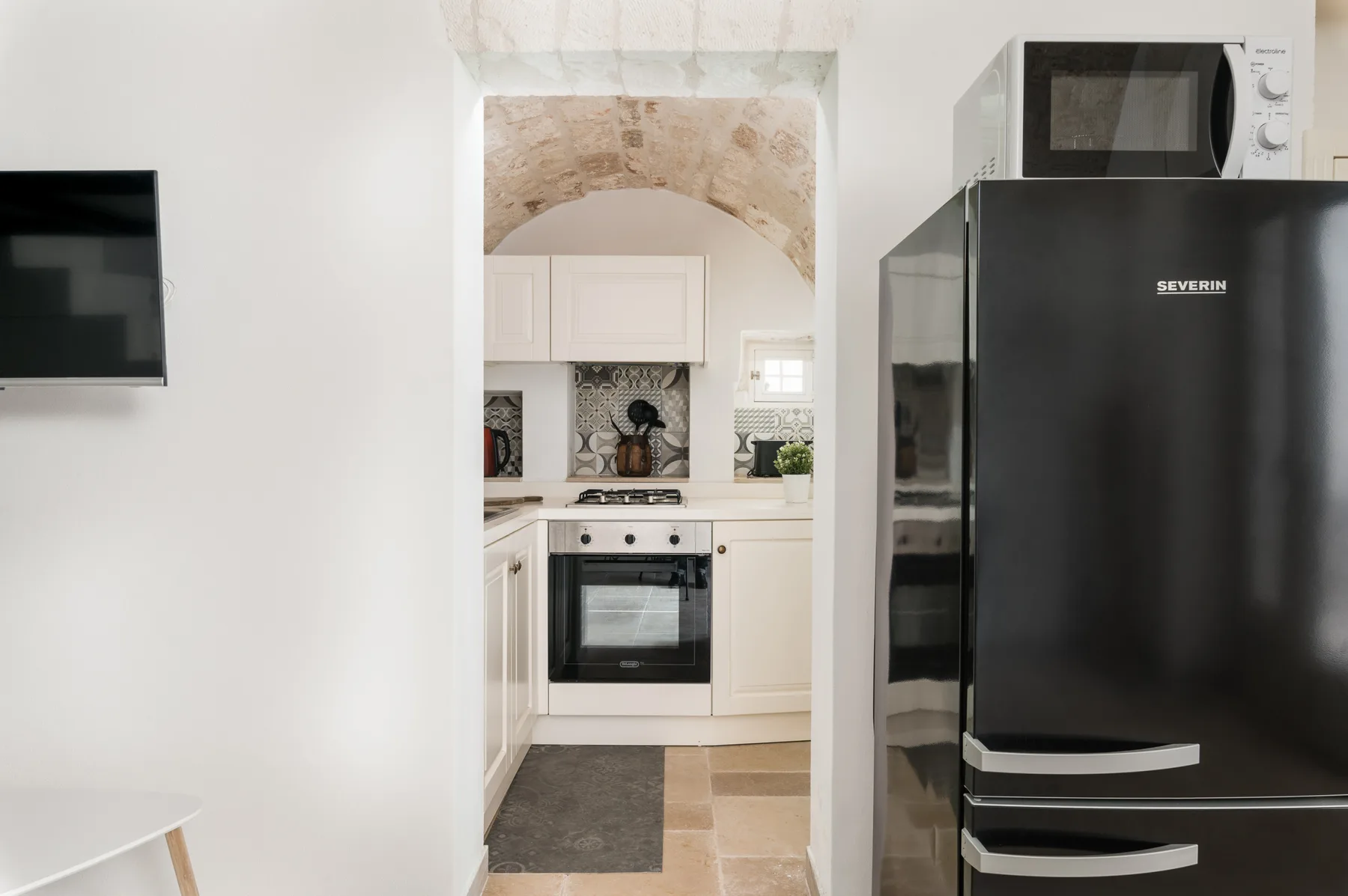 A compact kitchen with white cabinetry, an oven, and a black refrigerator.