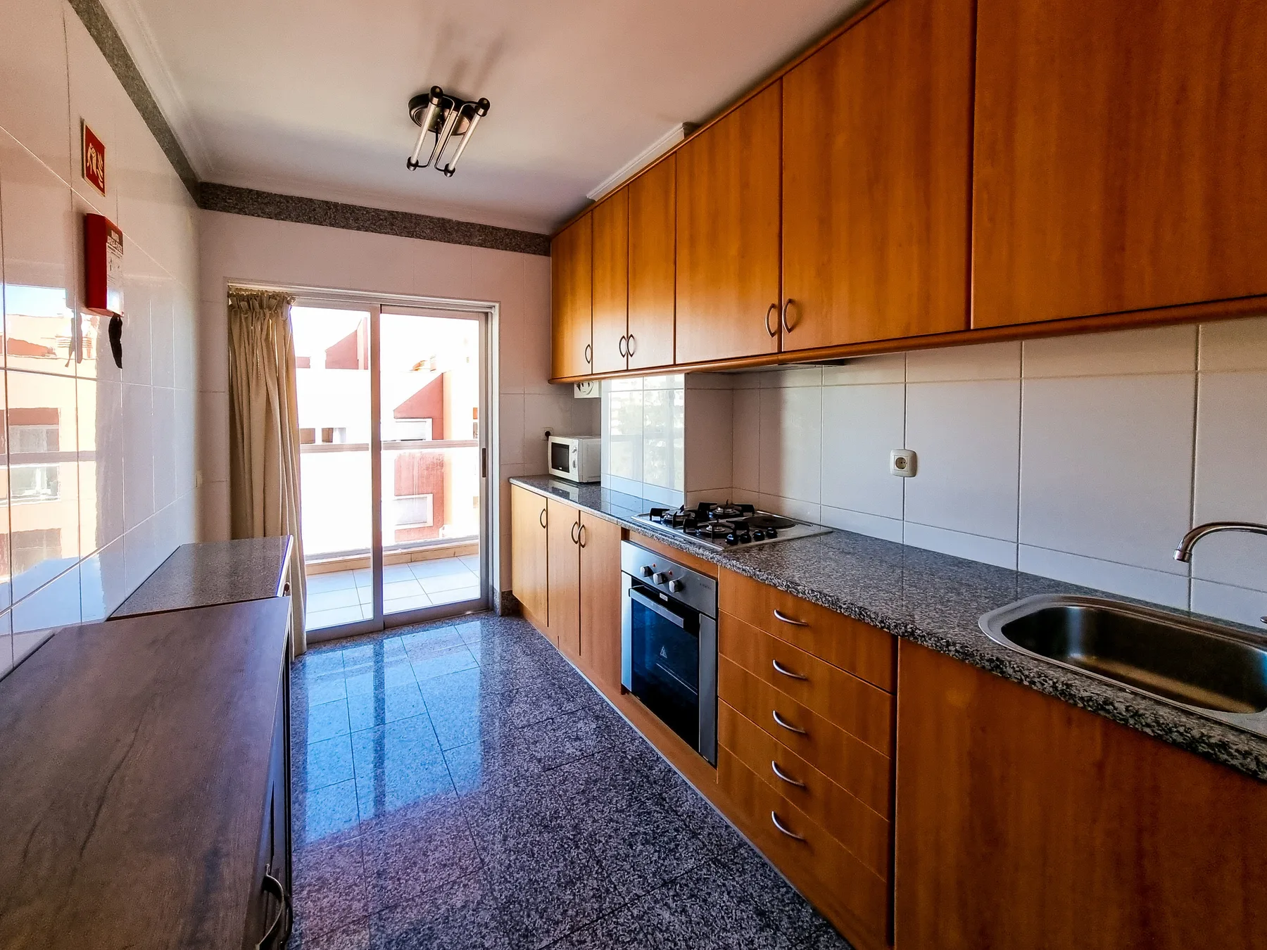Una cocina con gabinetes de madera, una encimera y una puerta de vidrio que da a un balcón.