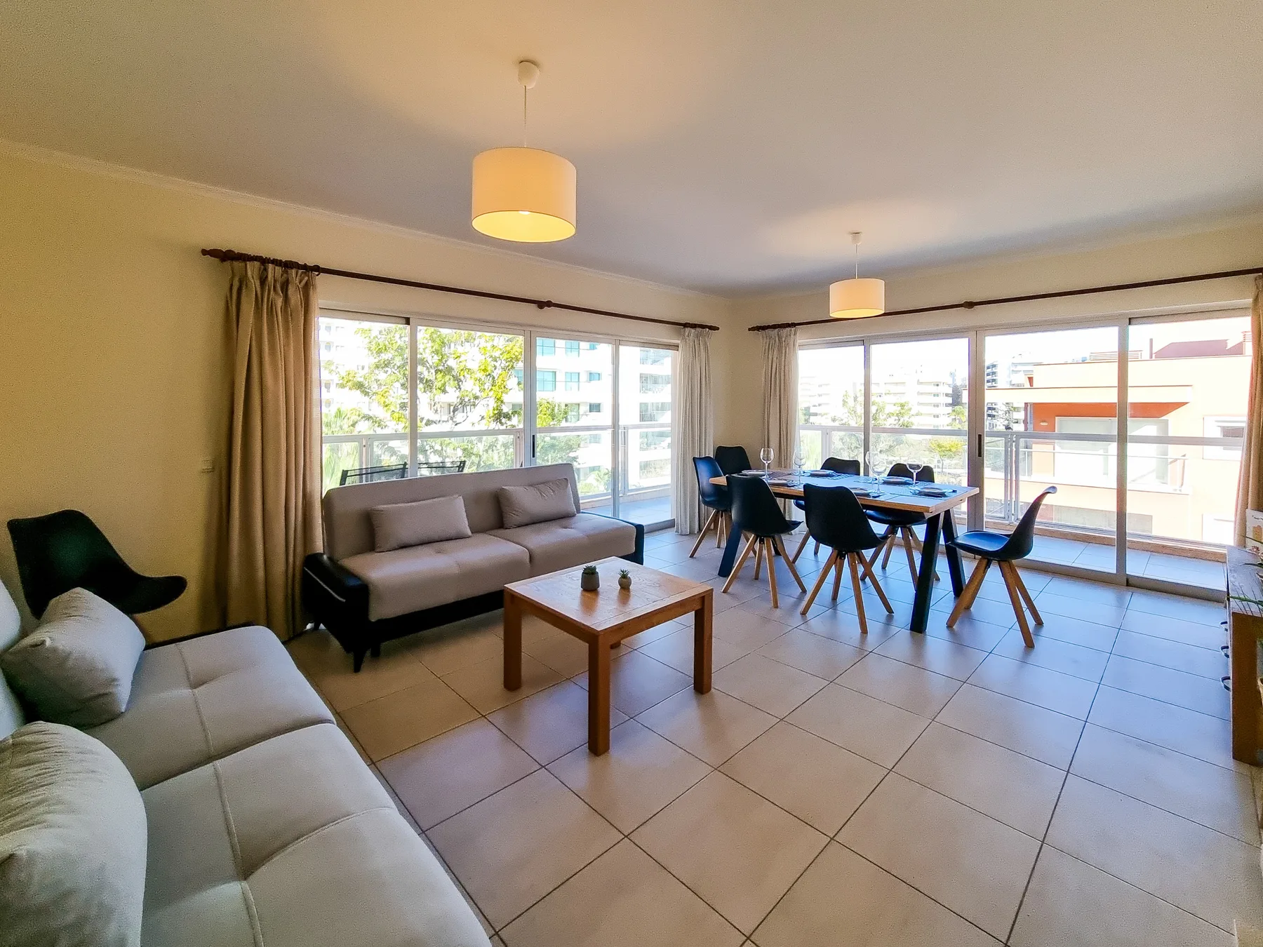 Una luminosa sala de estar y comedor con sofás, una mesa de centro y una mesa de comedor junto a grandes ventanas.