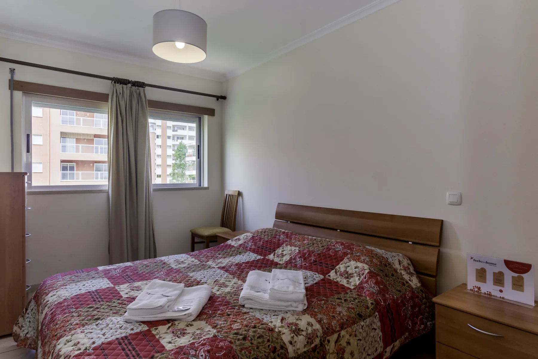 Un dormitorio con una cama cubierta por una colcha estampada y una ventana con cortinas.