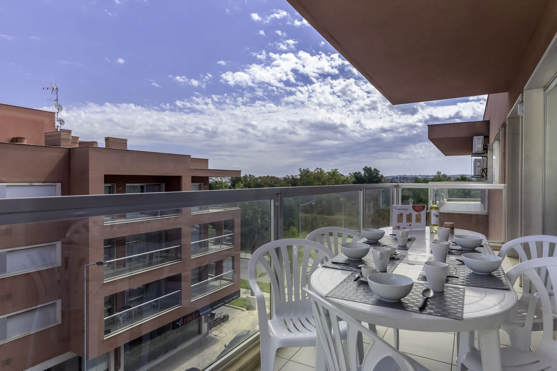 Comedor en un balcón con mesa y sillas, con vistas a edificios cercanos.