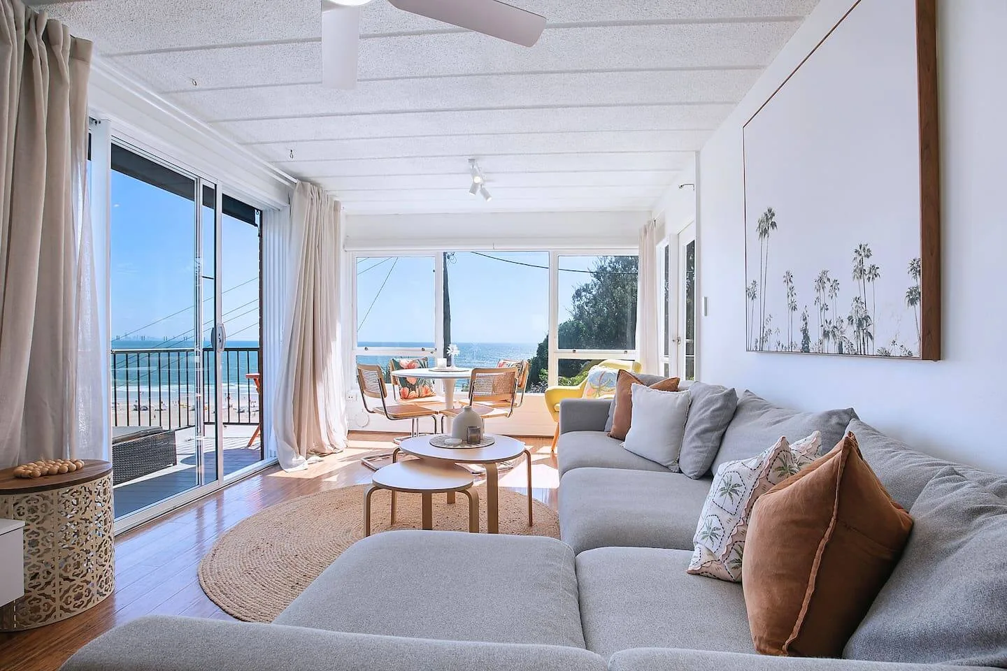 Una sala de estar luminosa tiene un sofá seccional grande, con el océano visible por las ventanas.