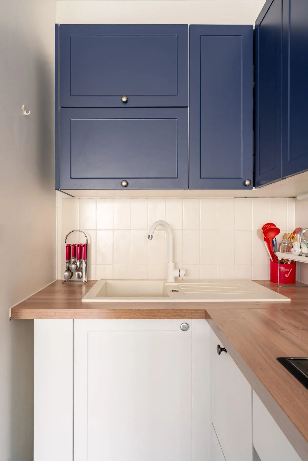 A compact kitchen with blue upper cabinets, white tile, and a wood countertop.