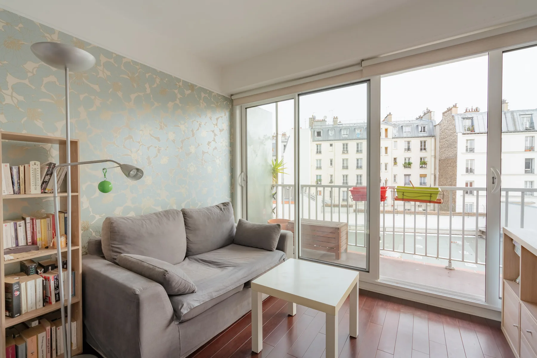 A bright living room with seating beside large windows overlooking nearby buildings.
