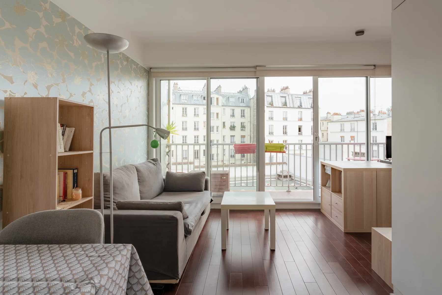 A bright living room with a sofa and large windows overlooking nearby buildings.