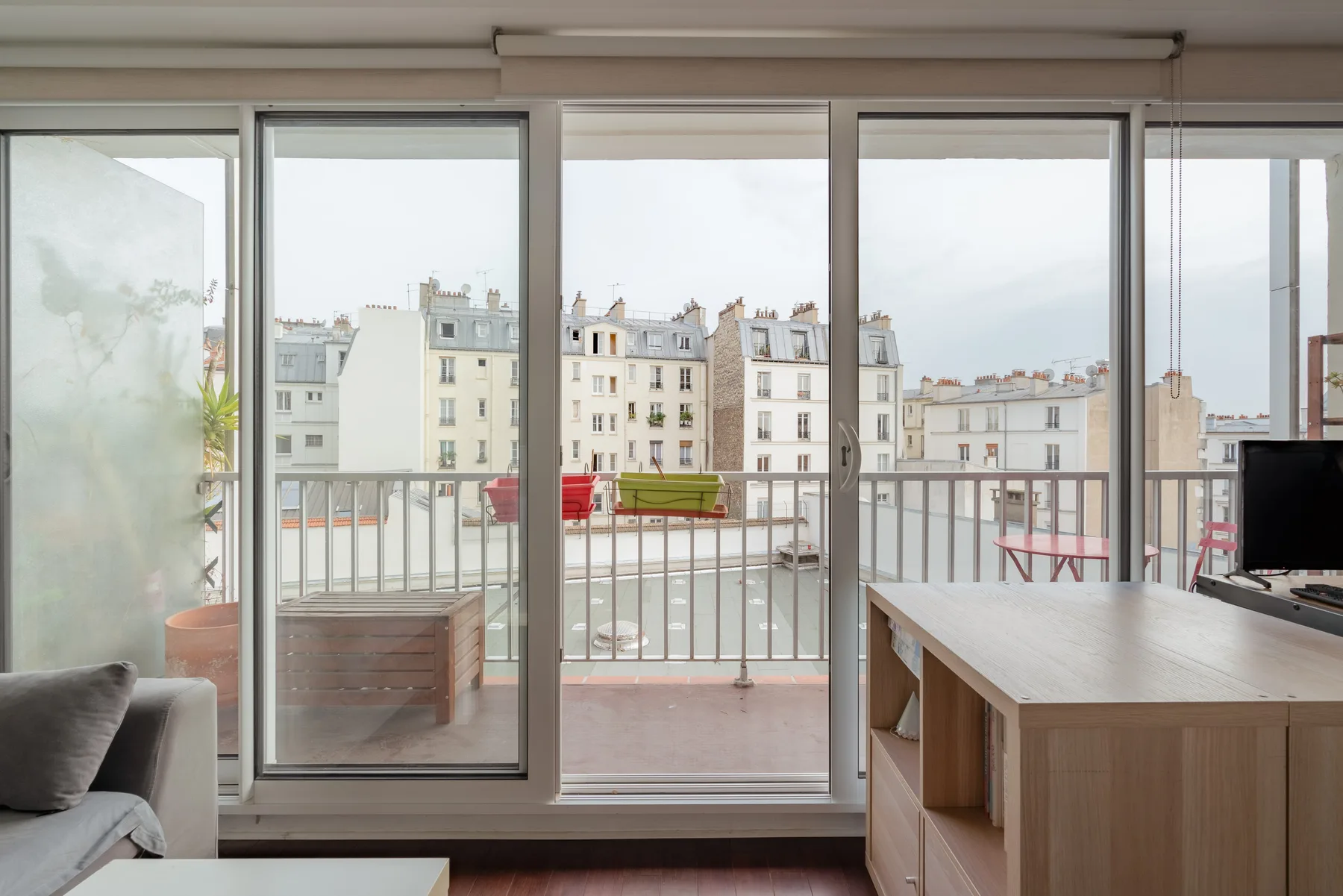 A bright living area opens onto a balcony overlooking neighboring apartment buildings.