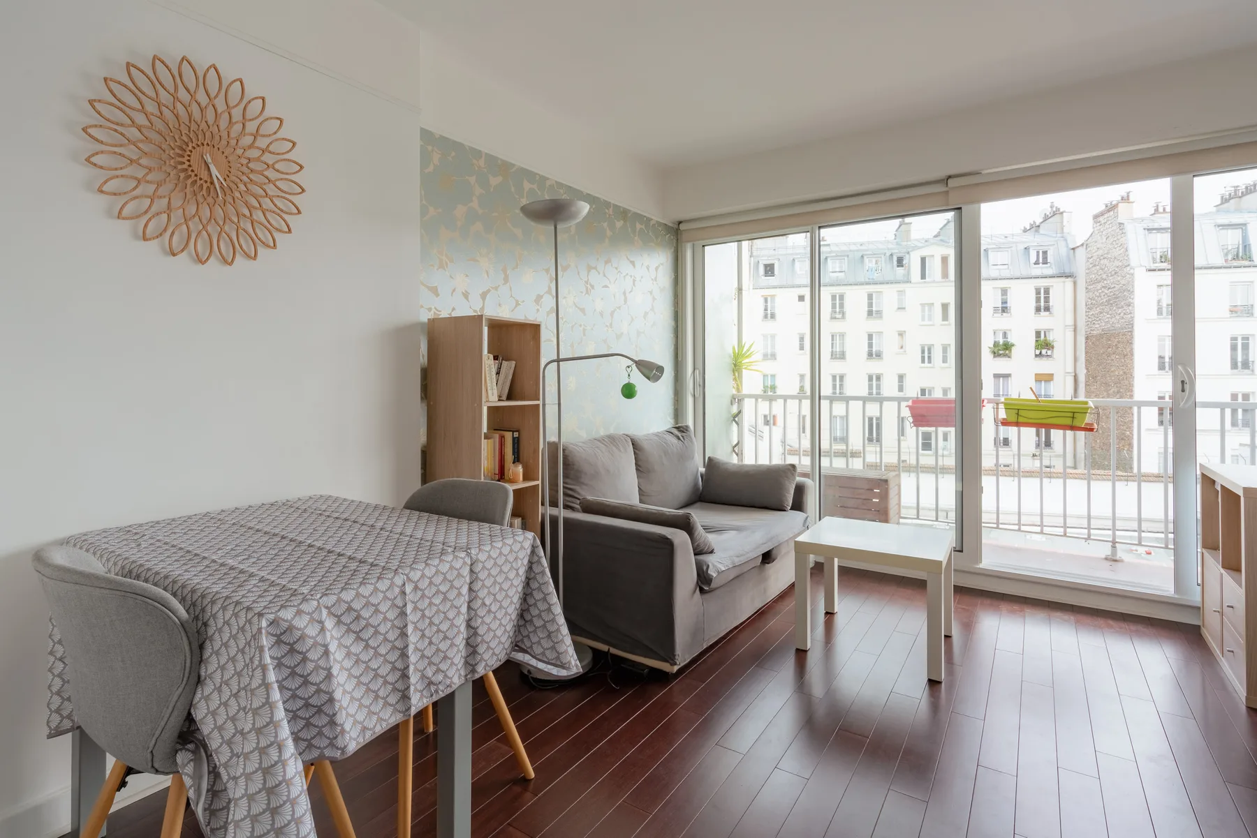 A bright living and dining area with seating and large windows overlooking neighboring buildings.