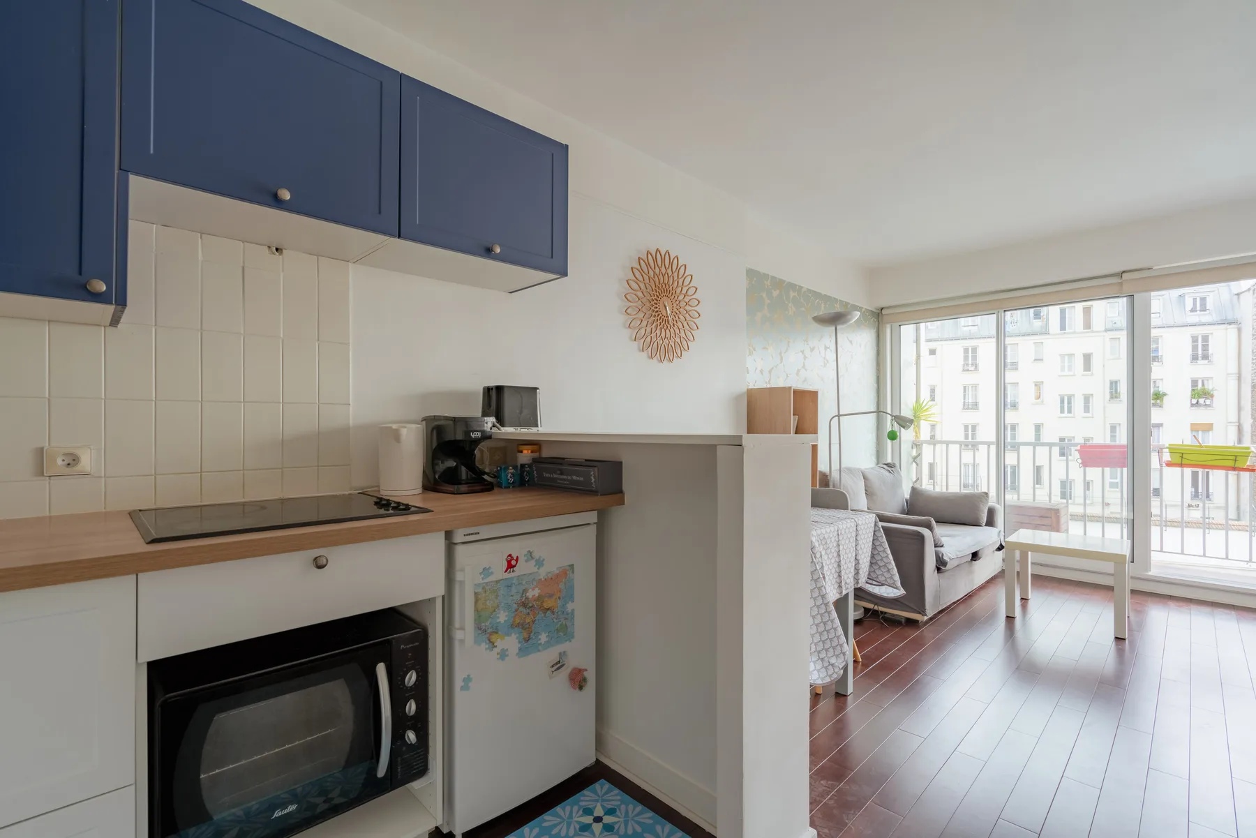 A compact kitchen opens into a bright living area with large windows.