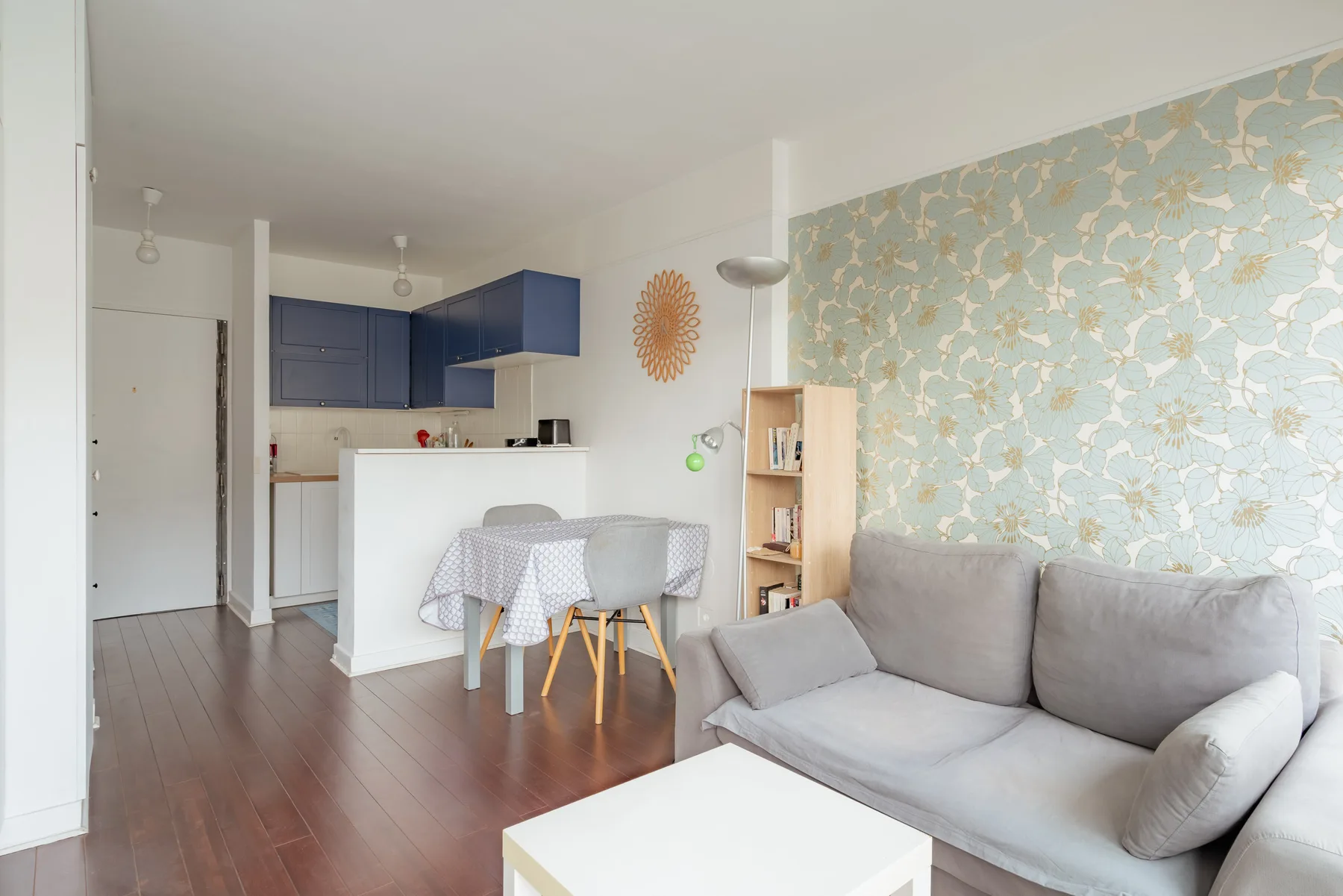 A living area with gray seating beside a compact kitchen.