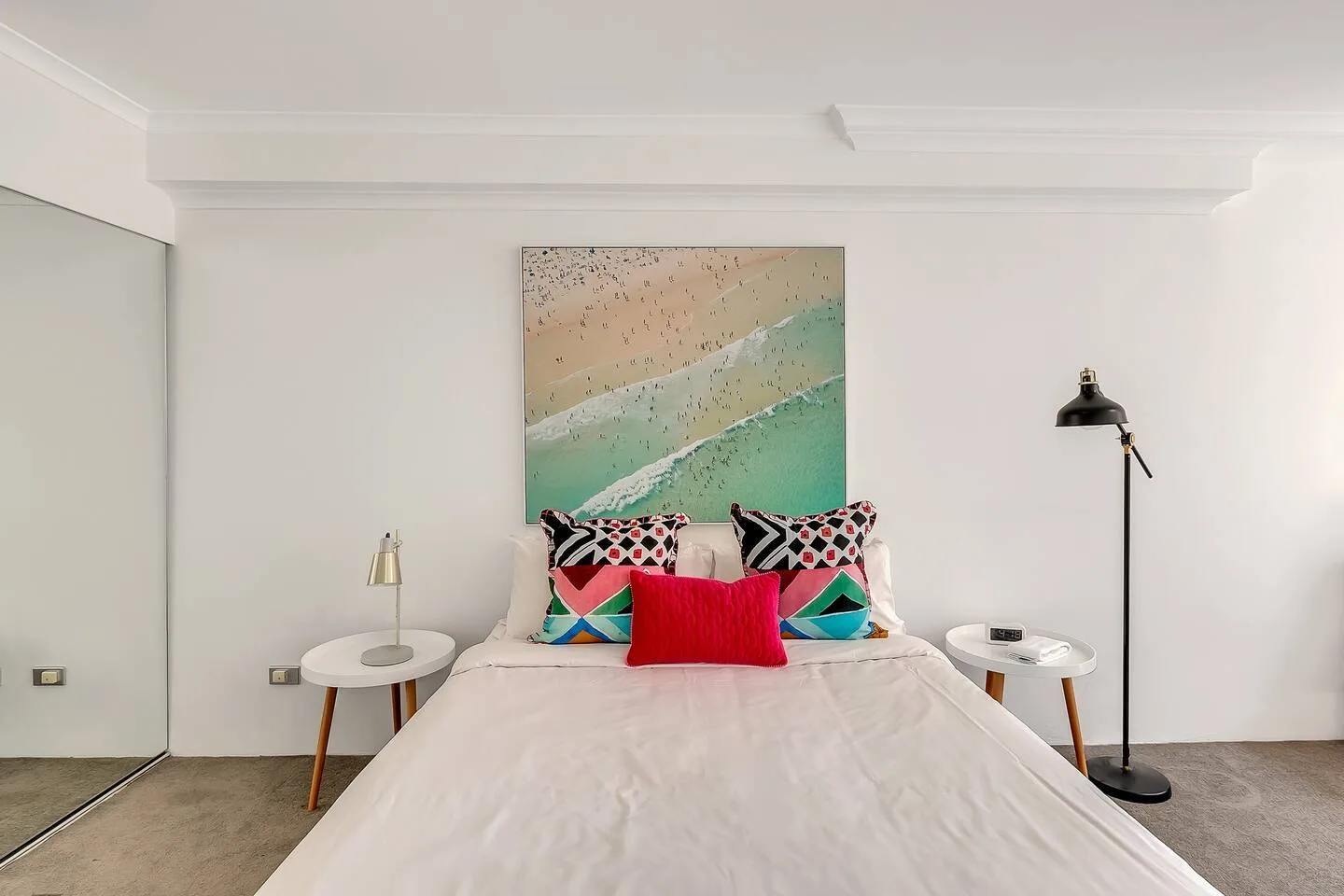 A bedroom with a bed, colorful pillows, and abstract artwork above the headboard.