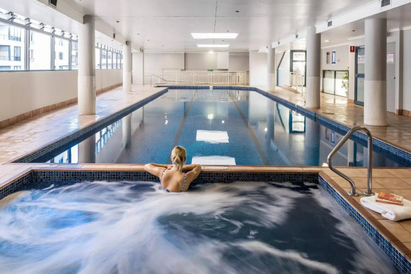 Una piscina cubierta y una bañera de hidromasaje comparten una sala luminosa con grandes ventanas.