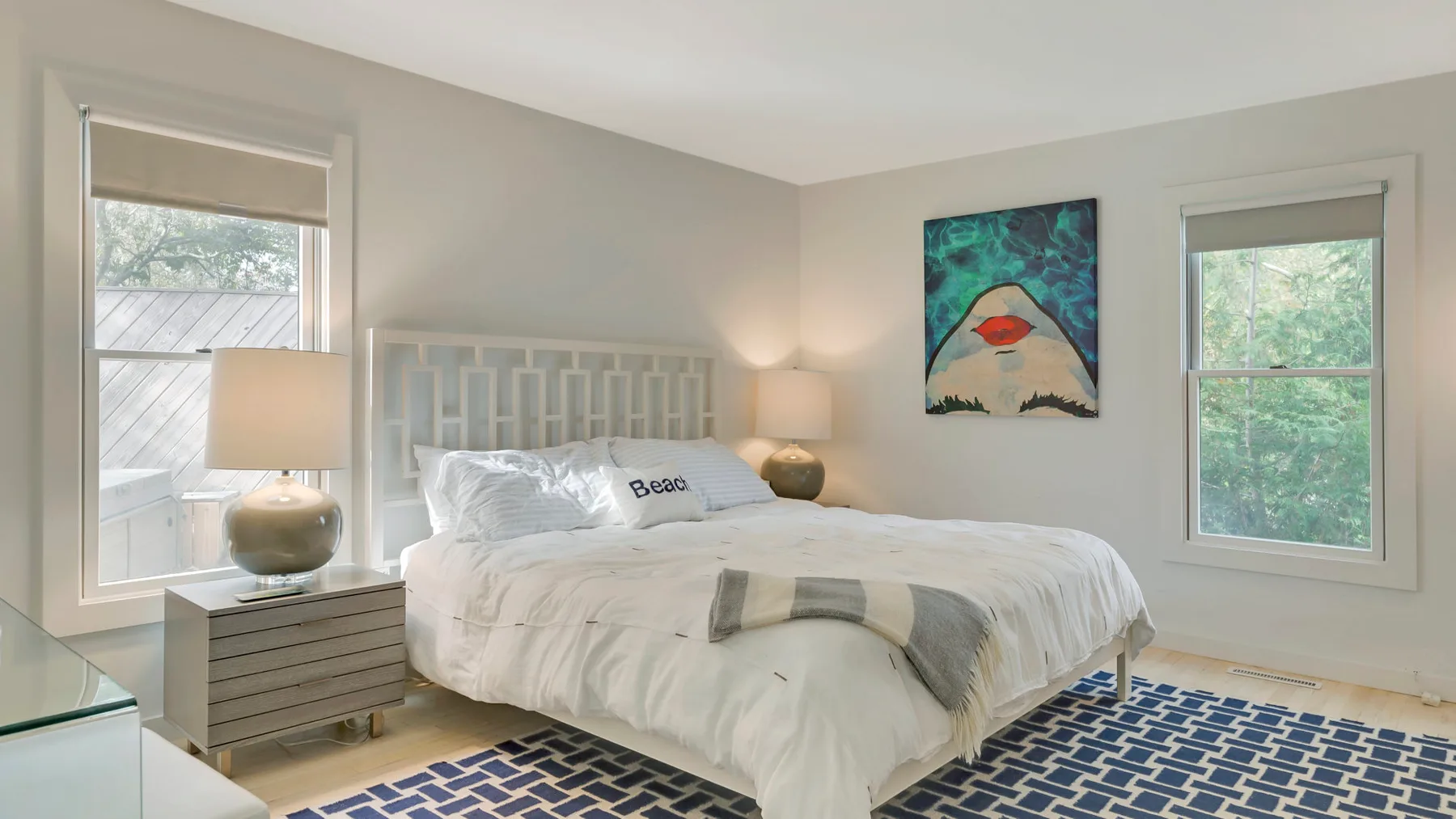 A bright bedroom with a bed, bedside tables, and colorful artwork on the wall.