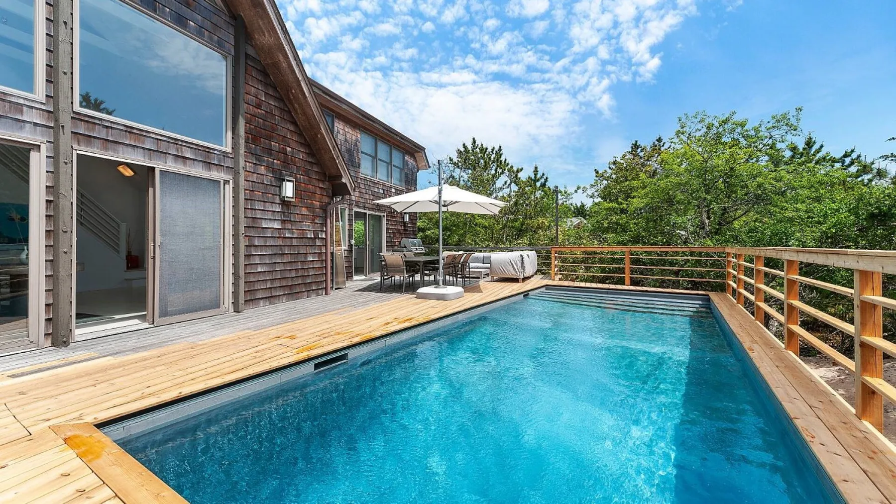 An outdoor swimming pool beside a wooden deck and house.