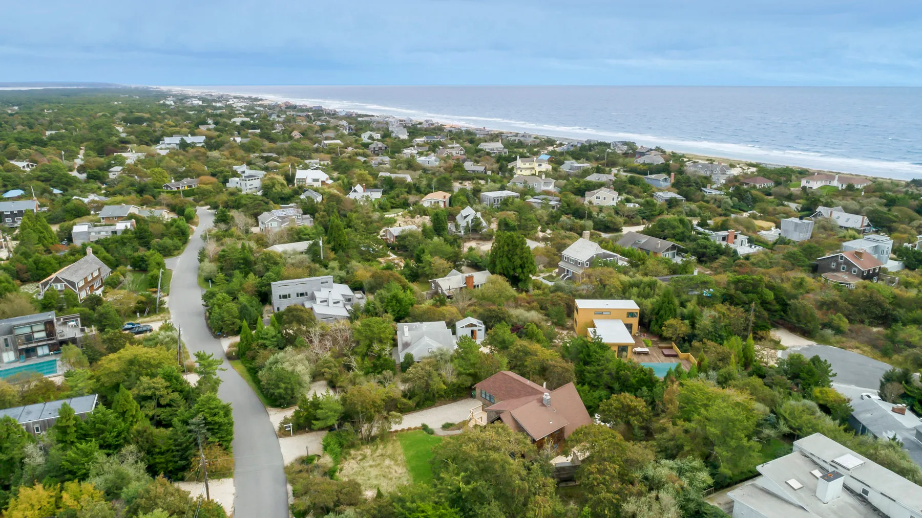 Aerial view of a coastal neighborhood with homes, greenery, and the ocean.