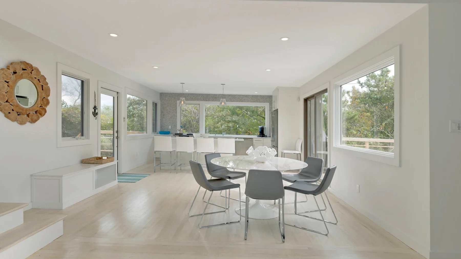 A bright dining area with a round table and a kitchen visible beyond.