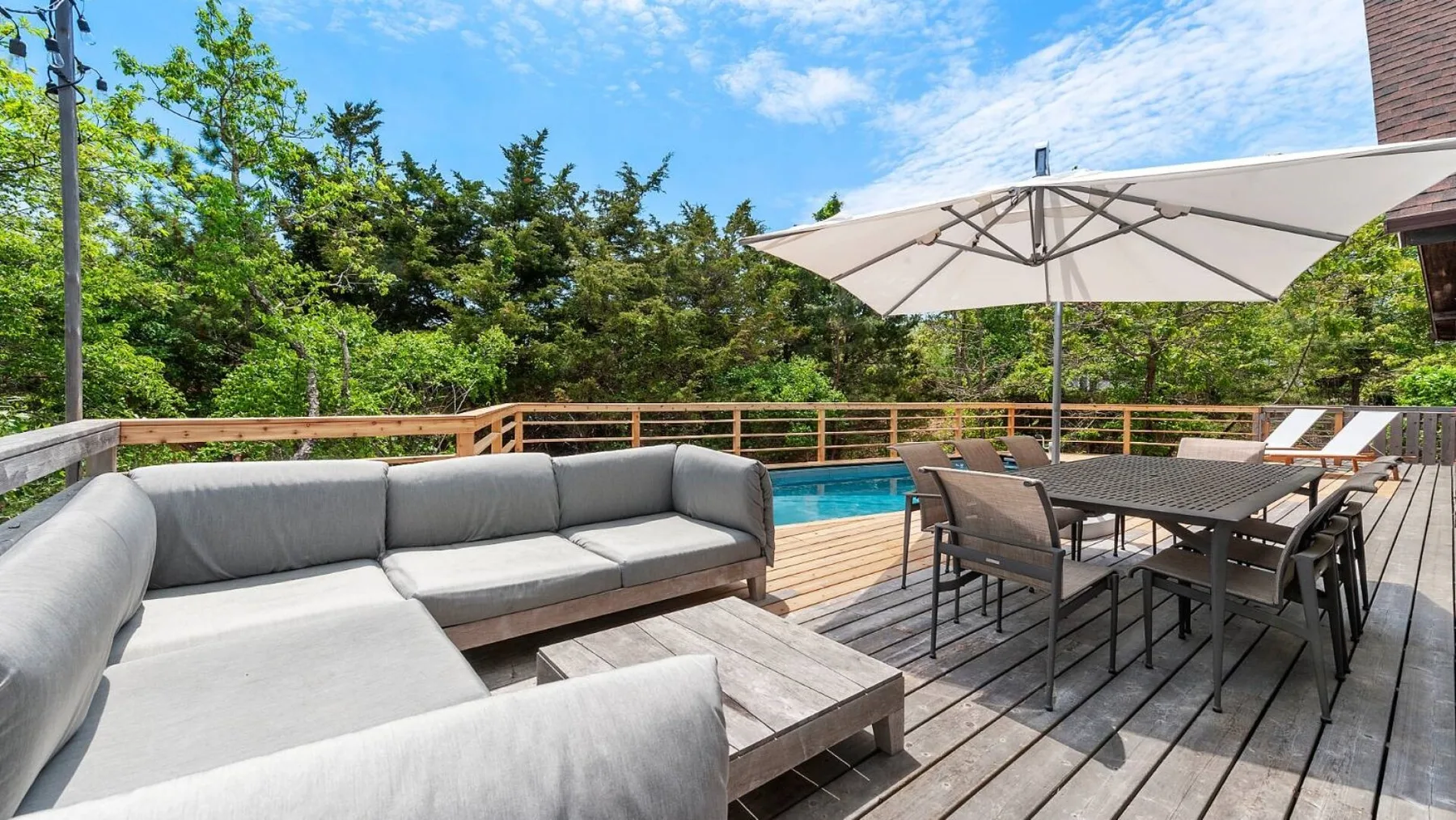 A wooden deck has outdoor seating, a dining table, and a pool.