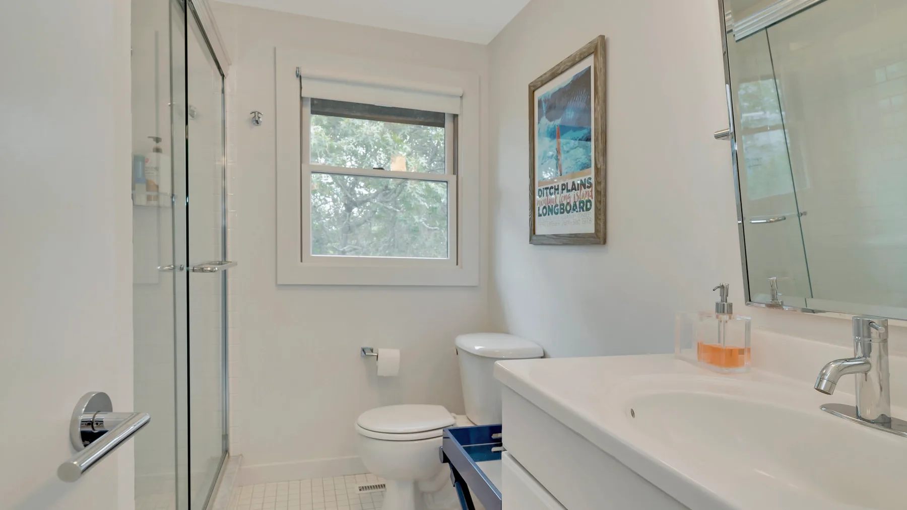 A bright bathroom with a glass shower, toilet, and sink.
