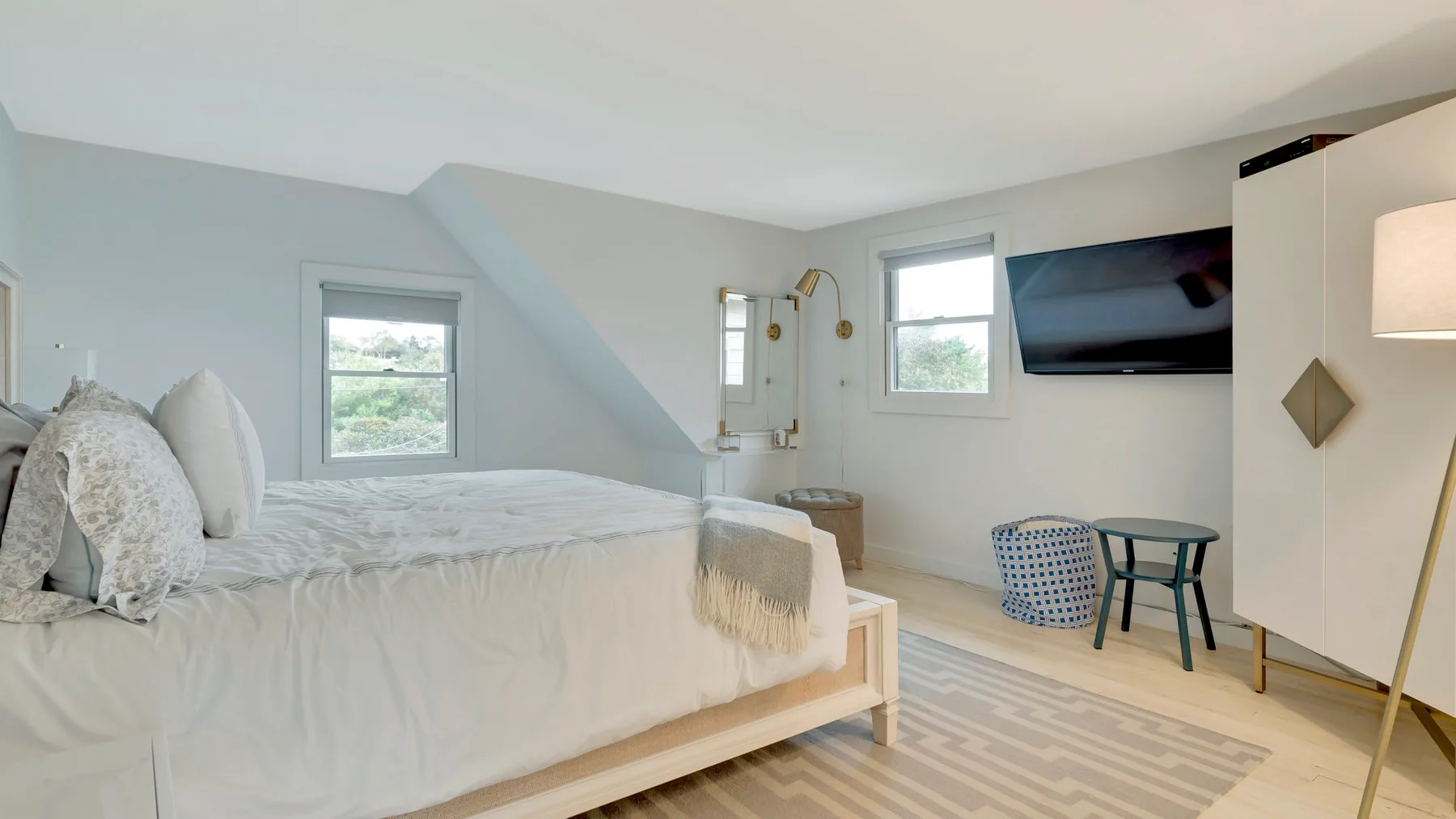 A bright bedroom with a neatly made bed and a wall-mounted television.