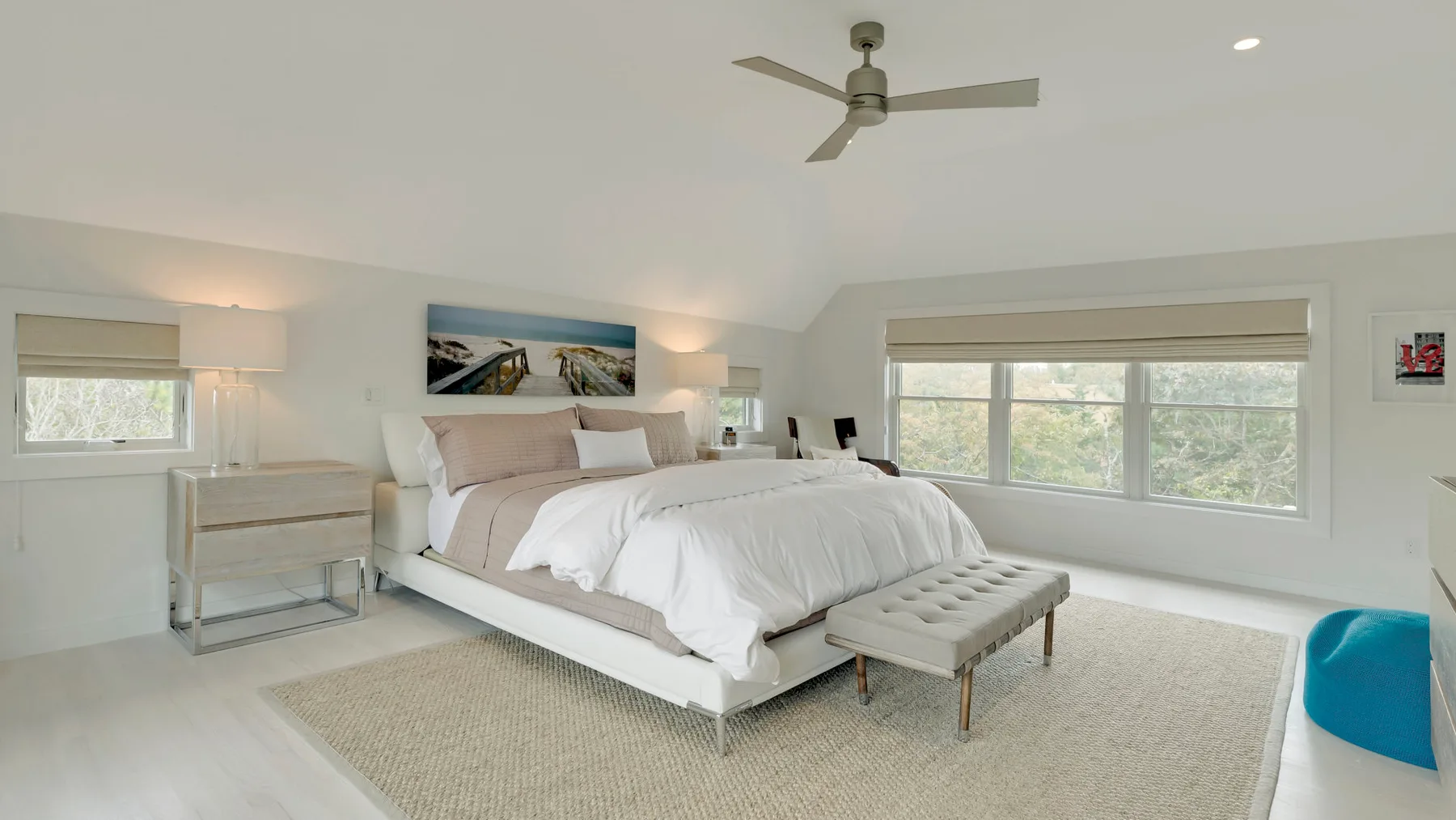 A bright bedroom with a large bed, bedside tables, and wide windows.