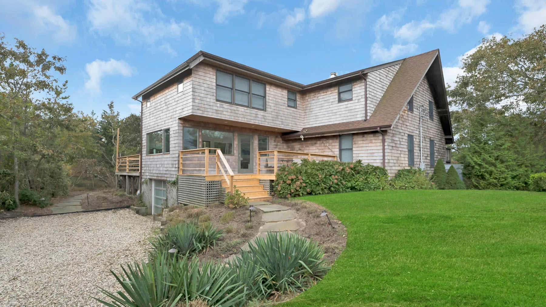A two-story house stands beside a green lawn and landscaped garden.