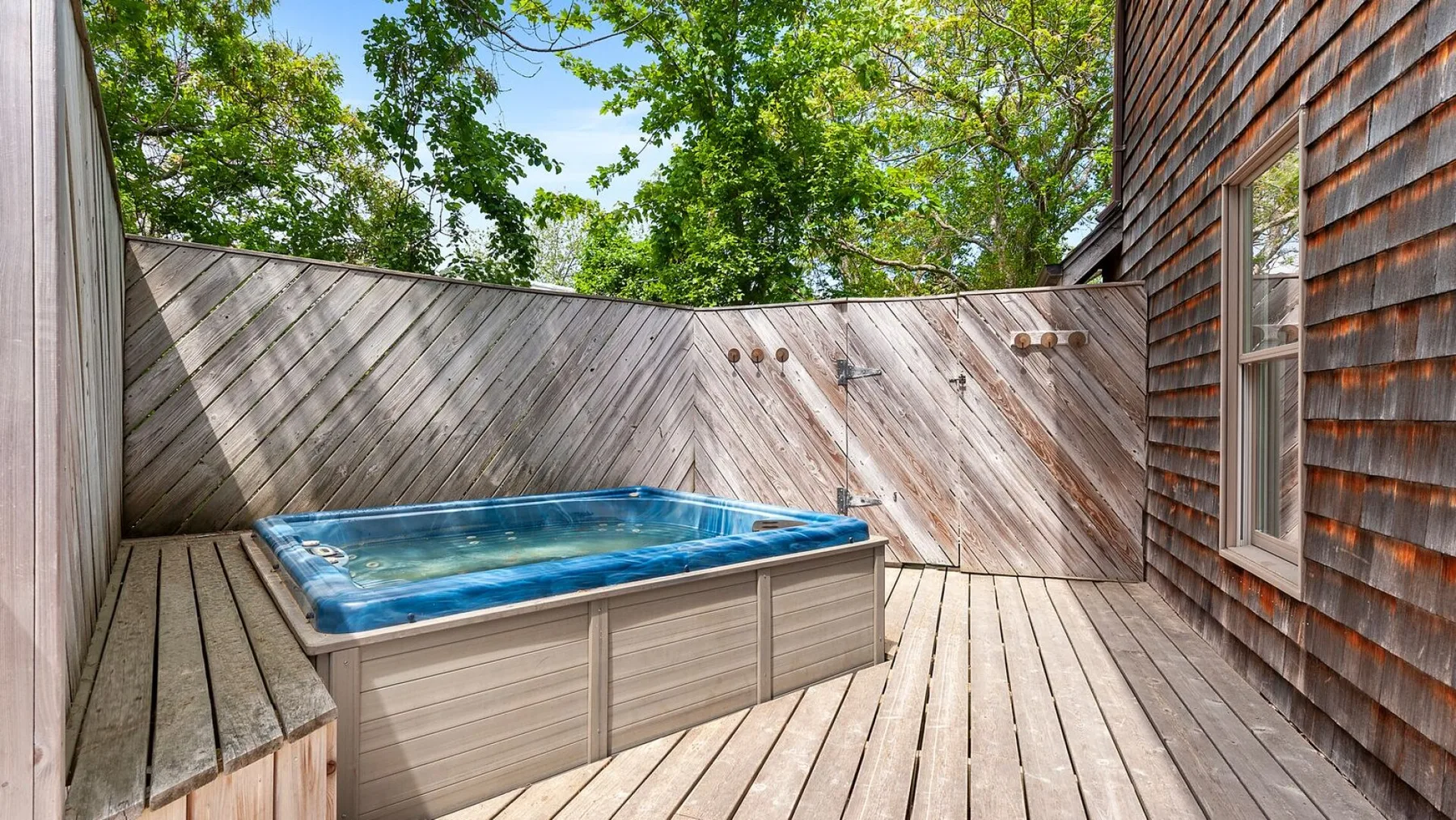 An outdoor deck features a blue hot tub beside wooden siding.