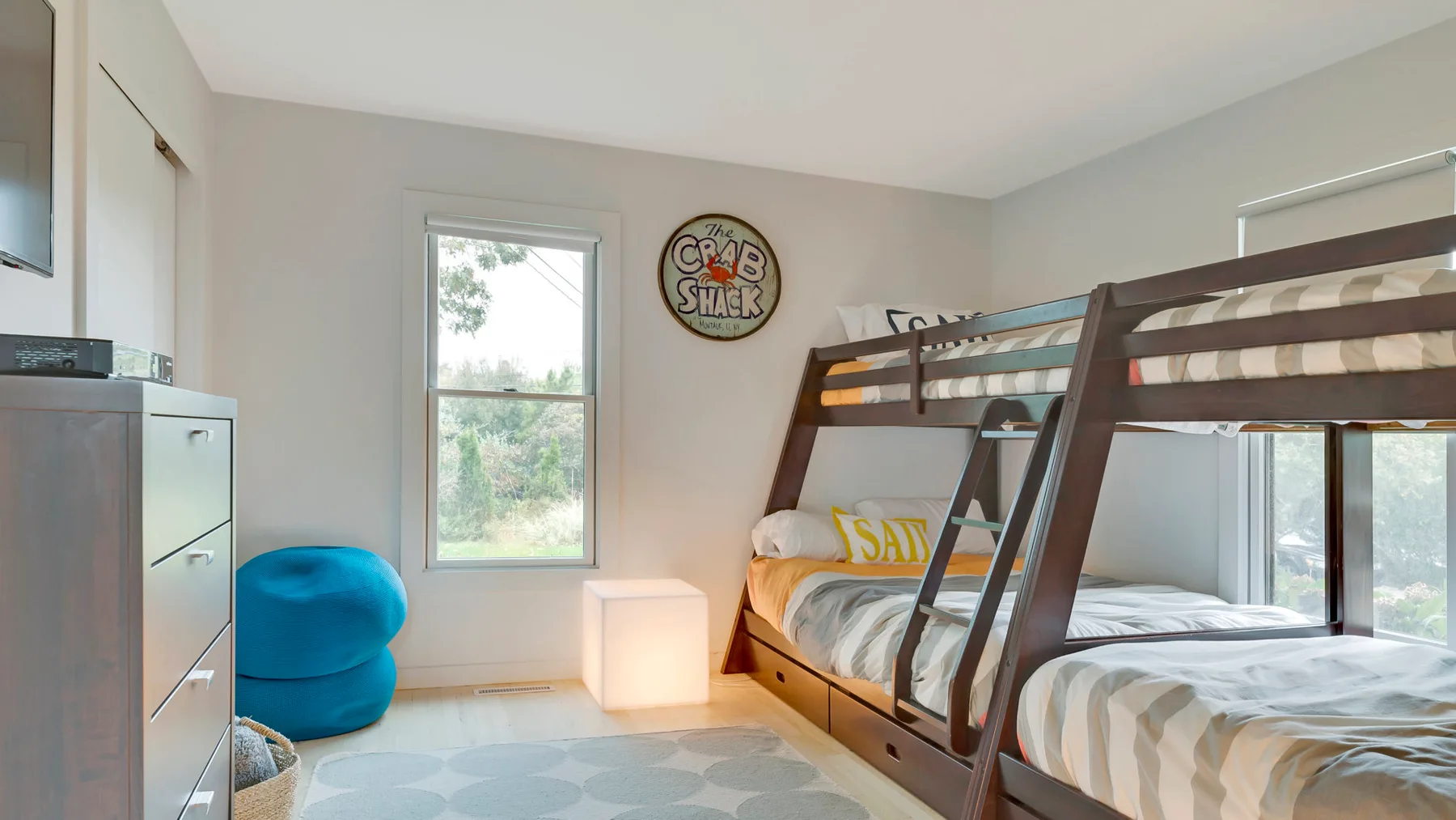A bedroom with a wooden bunk bed, a blue beanbag, and windows.
