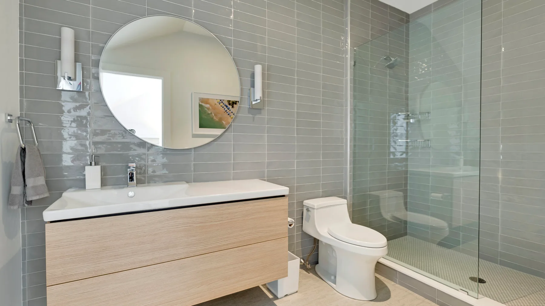 A modern bathroom with a vanity, round mirror, and glass shower.