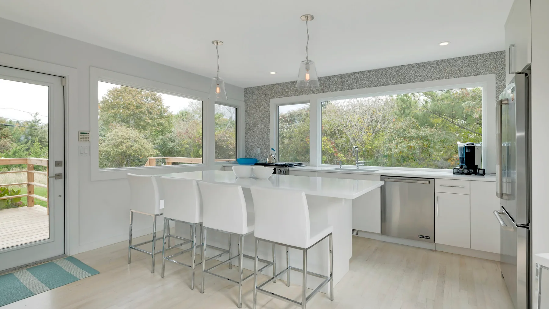 A bright kitchen with a white island and large windows overlooking greenery.