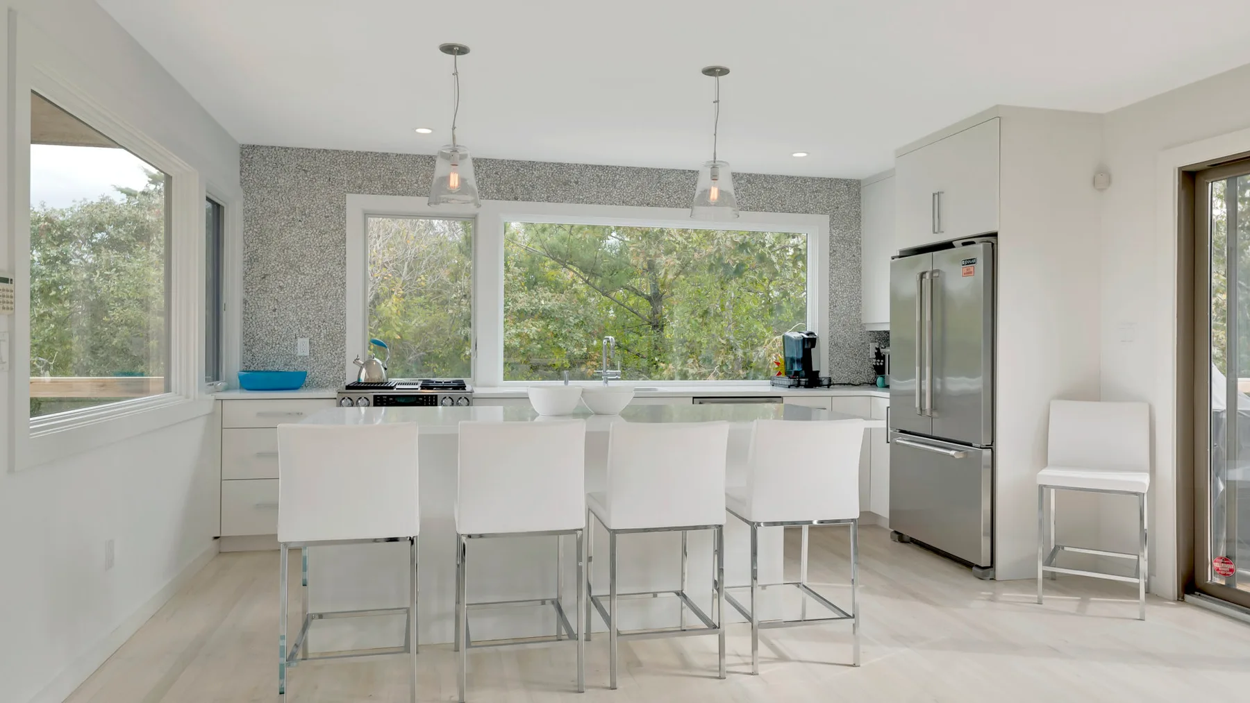 A bright kitchen with white cabinetry, a central island, and large windows.