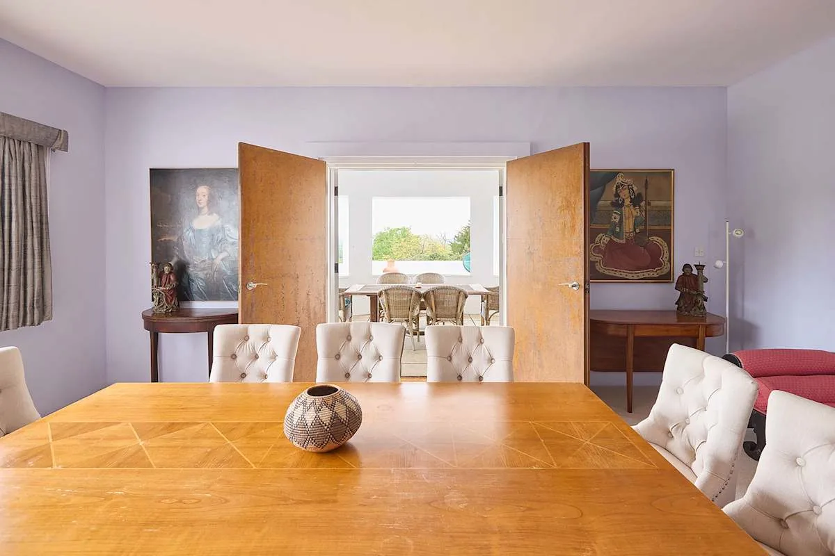 Un comedor con una mesa grande de madera y puertas dobles abiertas.