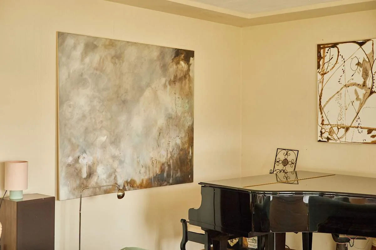 Un piano está bajo una obra abstracta en una sala de música con luz tenue.