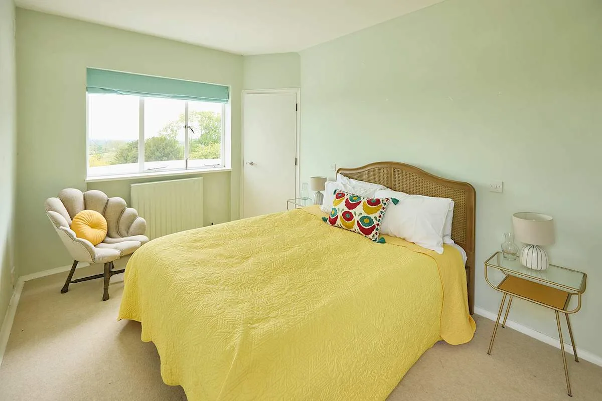 Un dormitorio con una colcha amarilla, una ventana y una pequeña zona para sentarse.