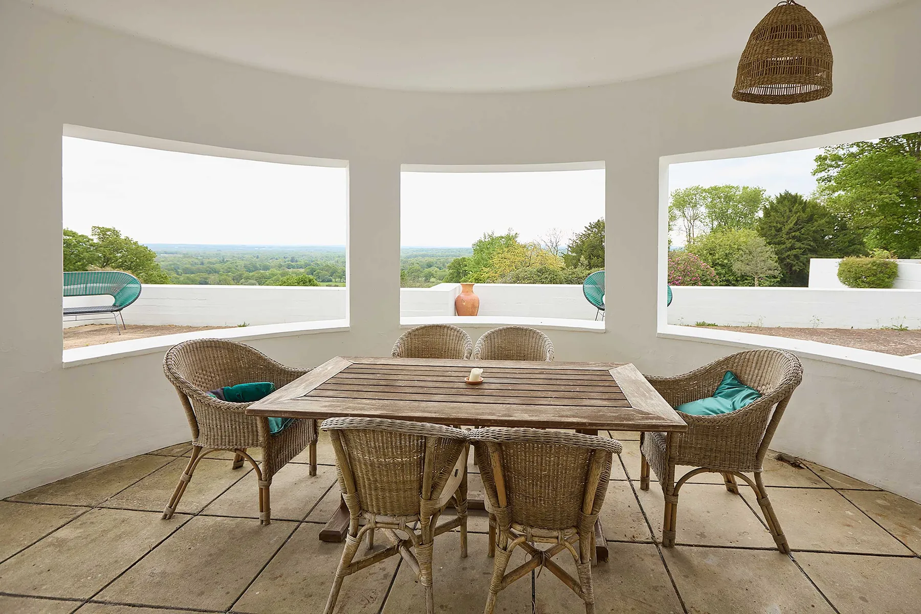 Comedor con una mesa de madera y asientos de mimbre junto a amplias ventanas.