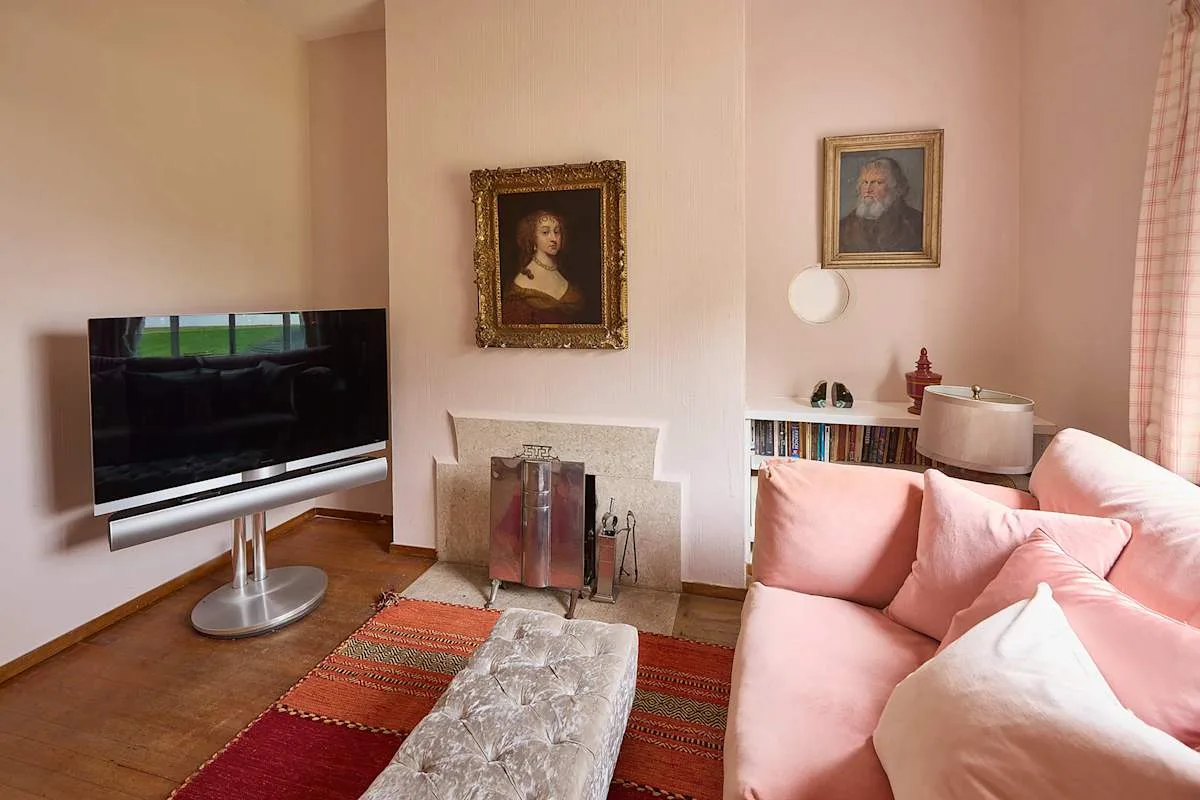 Una sala de estar con asientos rosas, un televisor y cuadros enmarcados.