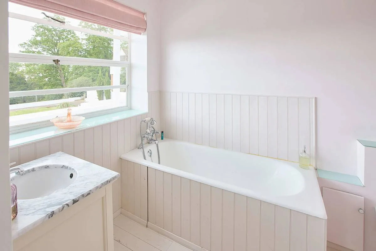 Un baño luminoso con una bañera y una ventana grande que da a zonas verdes.
