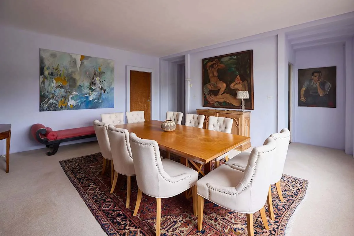 Un comedor con una mesa de madera, asientos tapizados y obras de arte en las paredes.