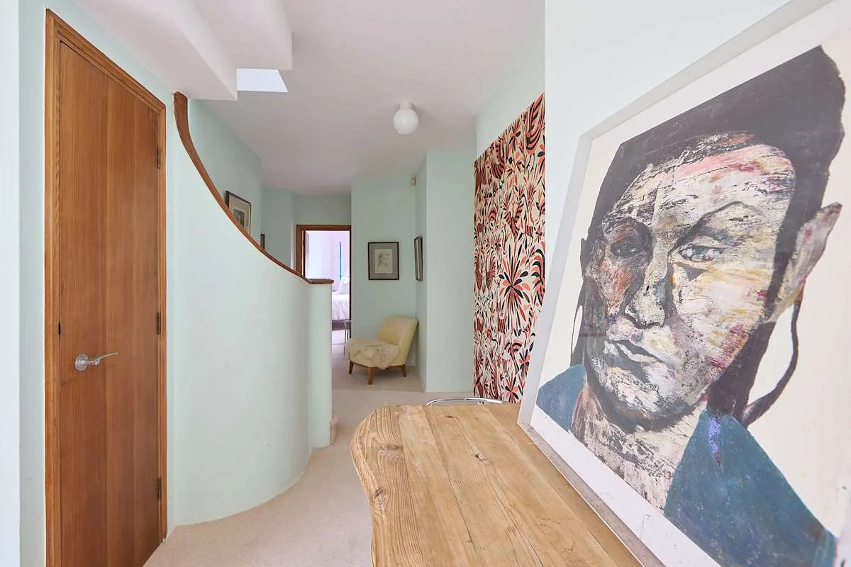 Un pasillo claro con una pared curva, una puerta de madera y un gran retrato.