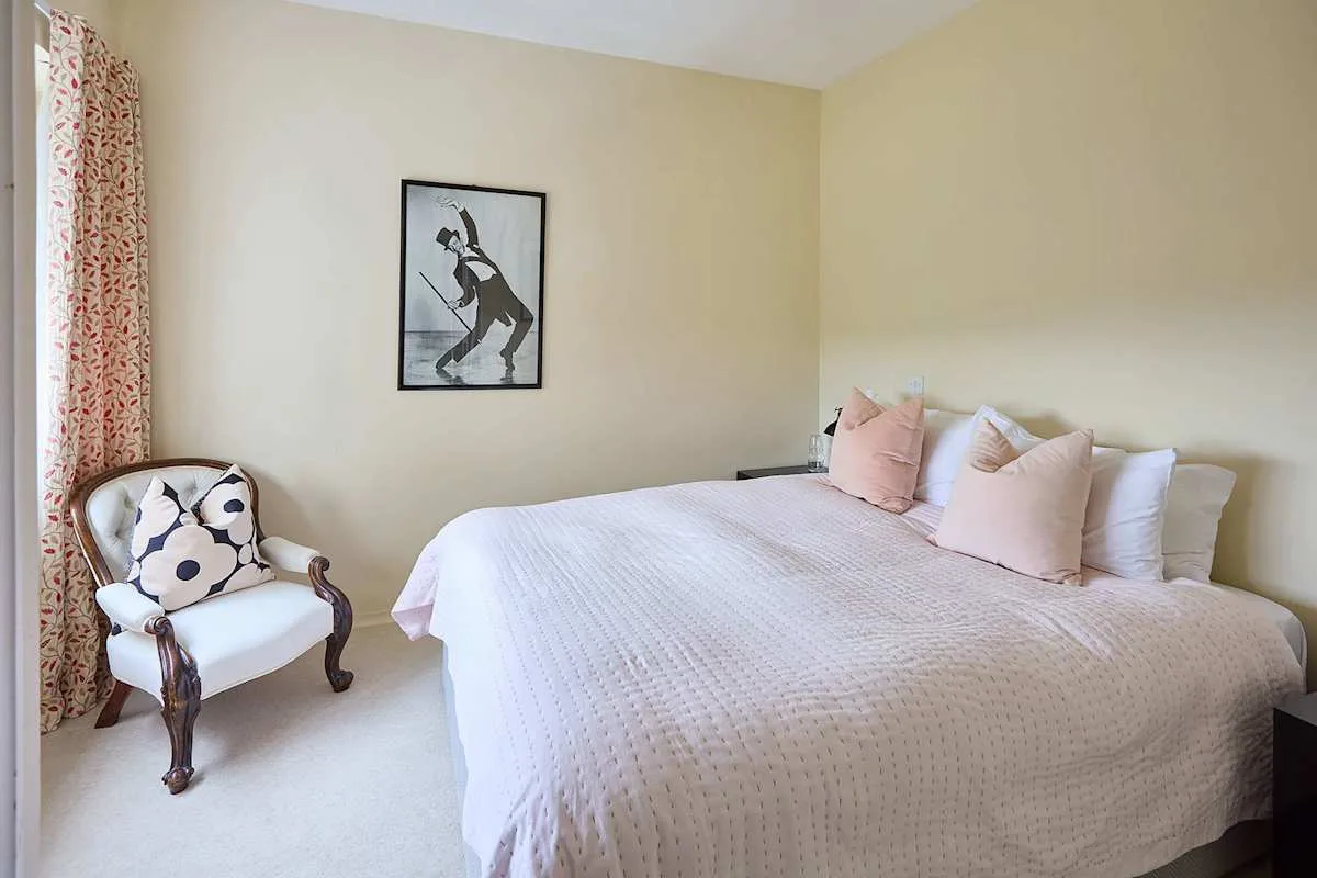 Un dormitorio con una cama tendida y un sillón tapizado junto a la ventana.