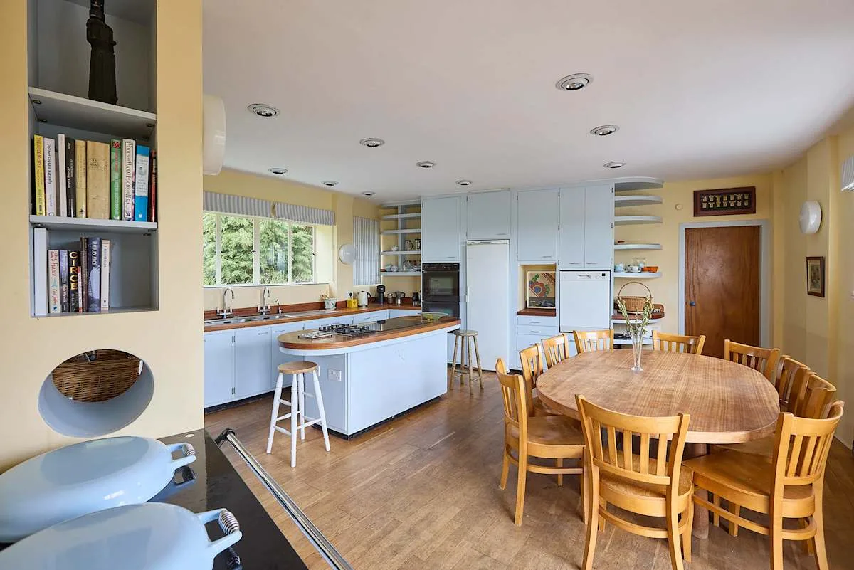 Una amplia cocina con comedor, mesa larga de madera e isla central.
