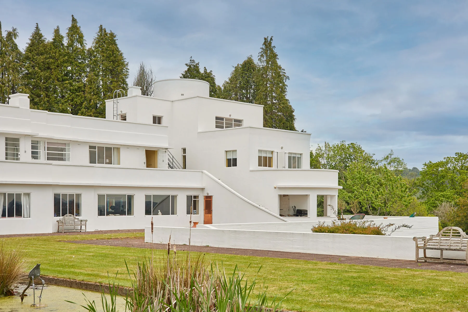 Un edificio blanco de estilo moderno da a un césped, con árboles altos detrás.
