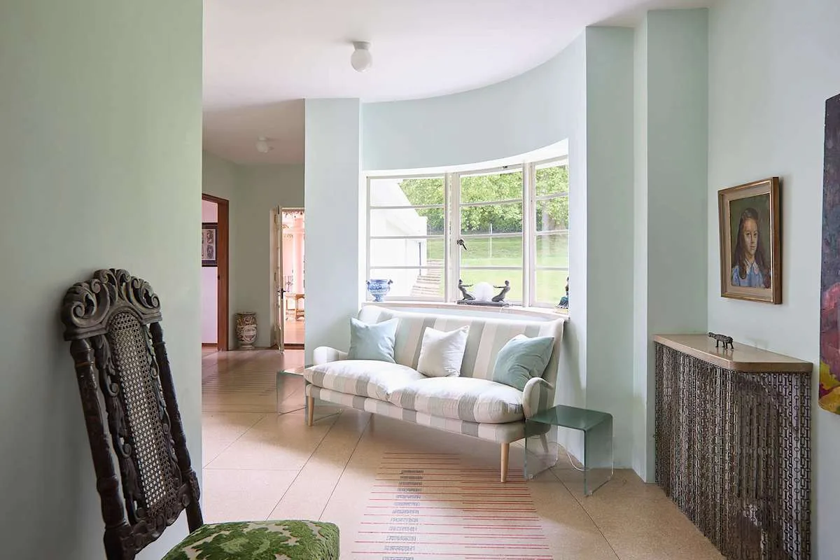 Una sala de estar luminosa con un sofá claro bajo una ventana grande.