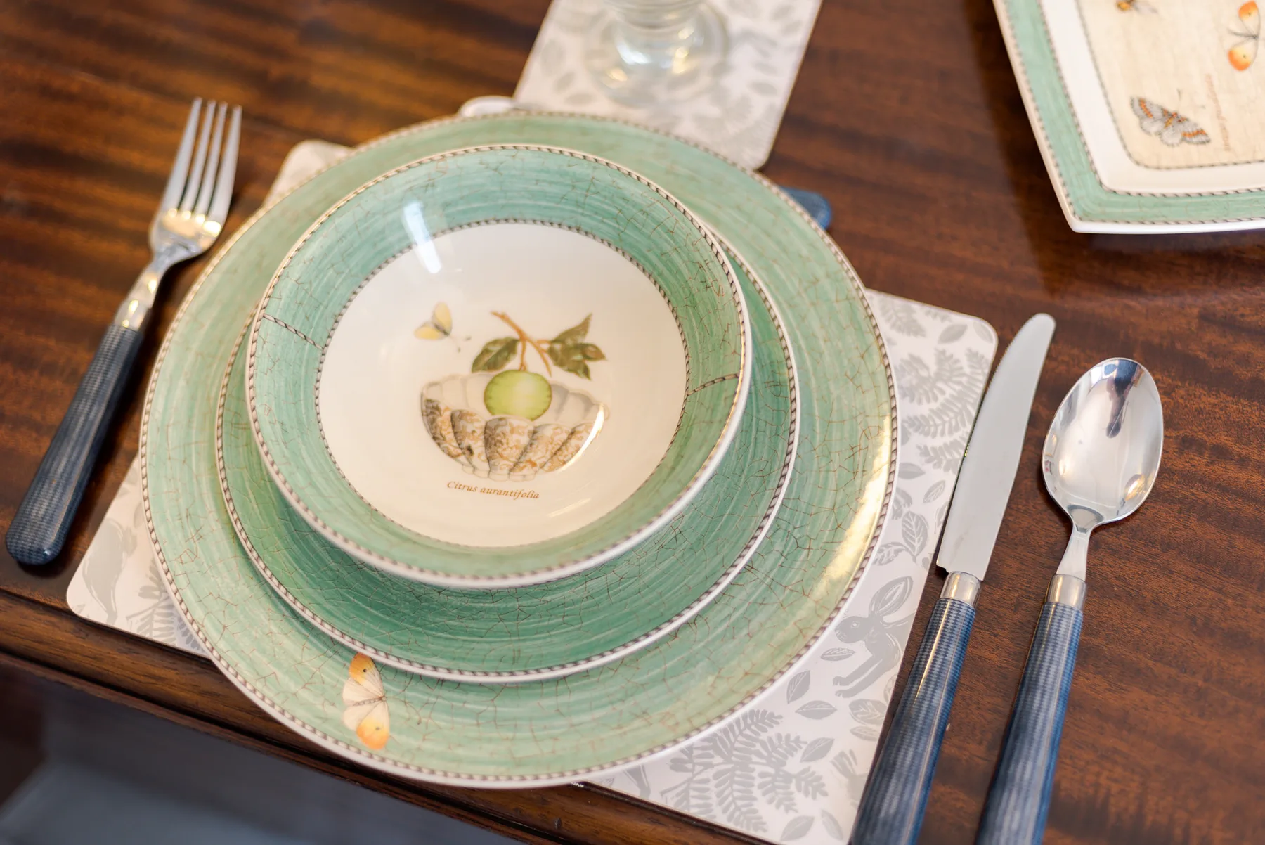A dining table set with green-rimmed plates, cutlery, and patterned placemats.