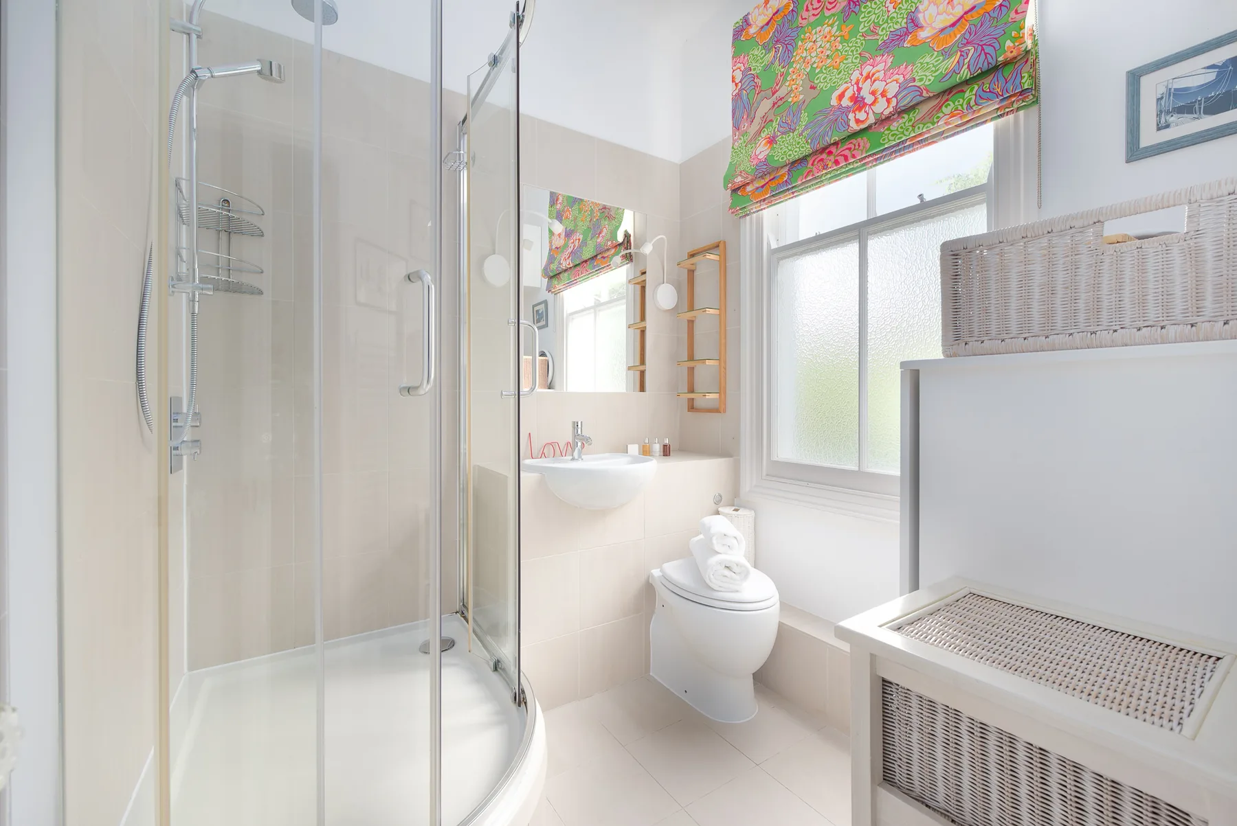 A bright bathroom with a glass shower, sink, and toilet beside a window.
