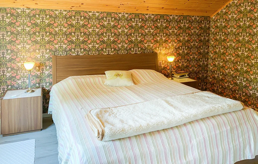 A bedroom with a bed, patterned wallpaper, and wooden ceiling.