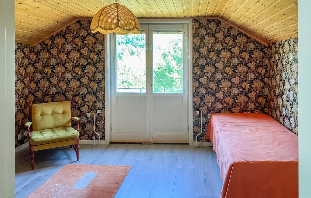 A bedroom with a single bed, armchair, and glazed doors at the far end.
