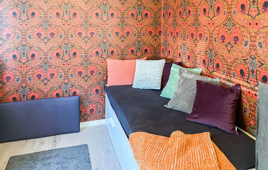A colorful bedroom with patterned walls and a bed covered in cushions.