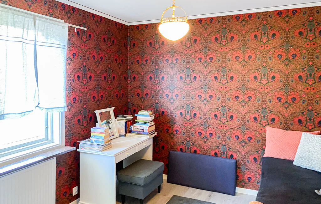 A small room with patterned red wallpaper, a desk, and a window.
