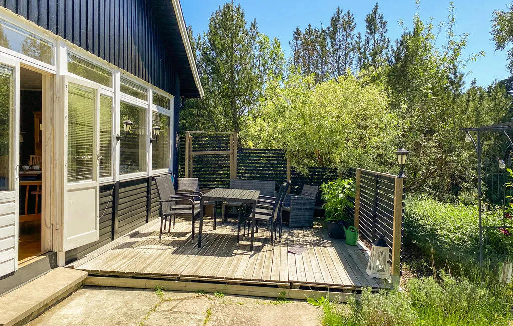 An outdoor deck with a table and seating beside a house, surrounded by greenery.